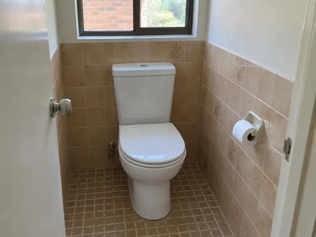 Clean white toilet in a small tiled bathroom with a window in Cranebrook
