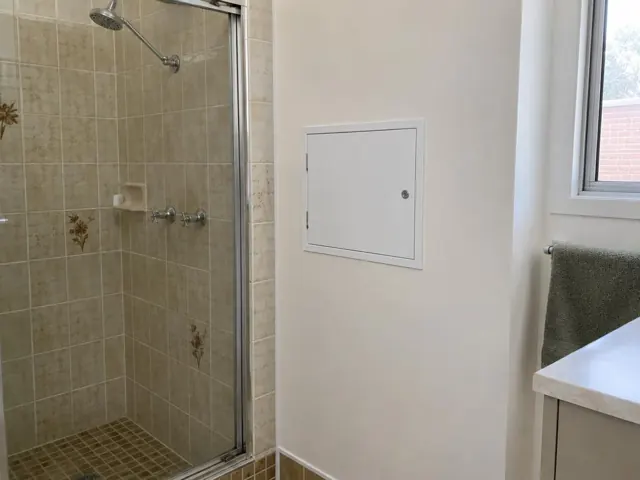 Small white access panel on a bathroom wall beside a shower and window in Jamisontown